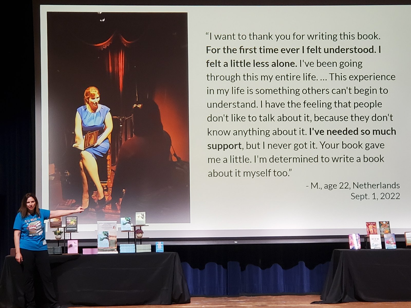 Amanda LaPera presenting to a large audience with a reader testimonial on screen.